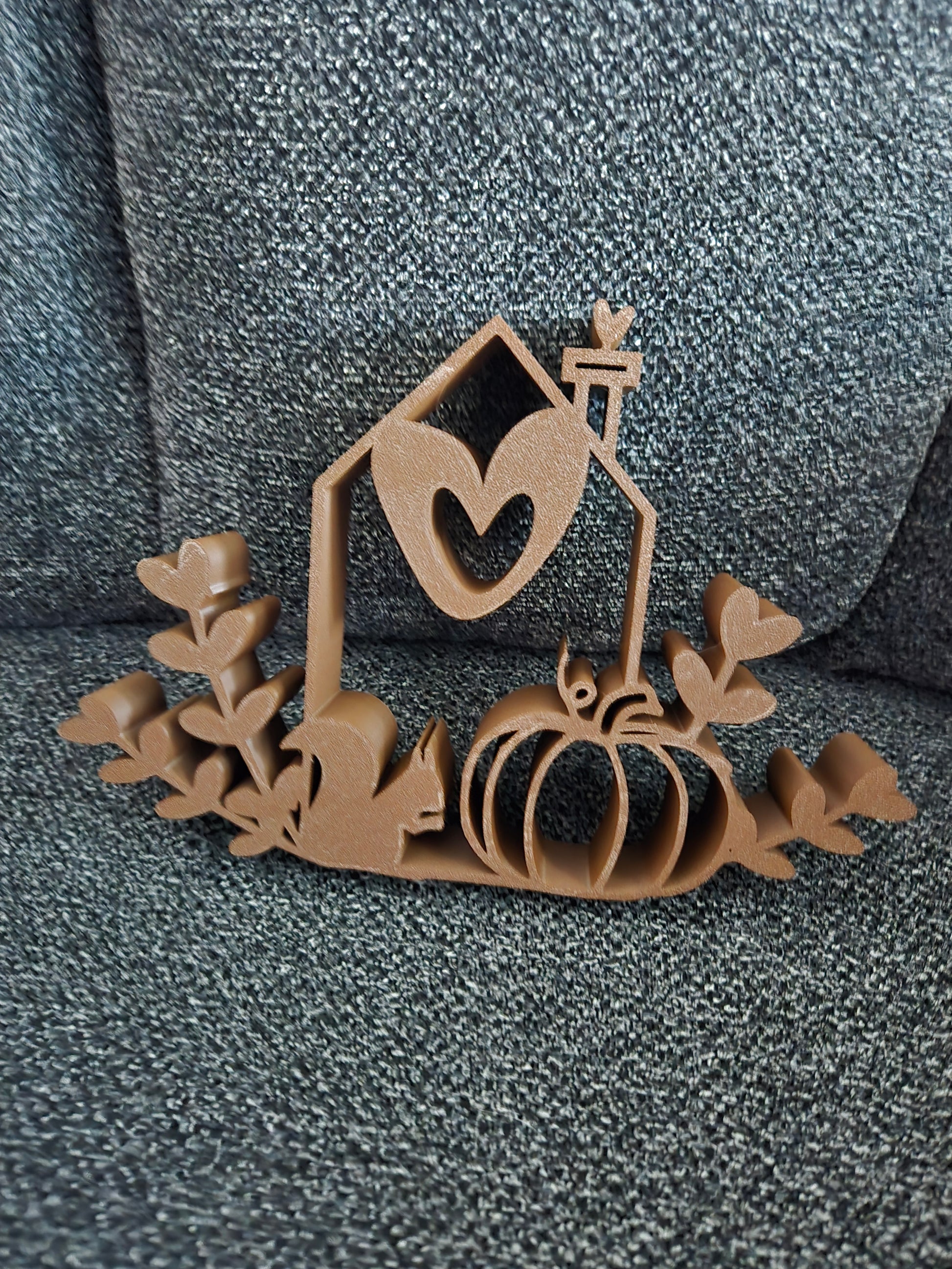 3D printed Home Sweet Harvest House in warm brown filament showing open-frame cottage silhouette with heart window, lantern, pumpkin, and ivy leaves, front view